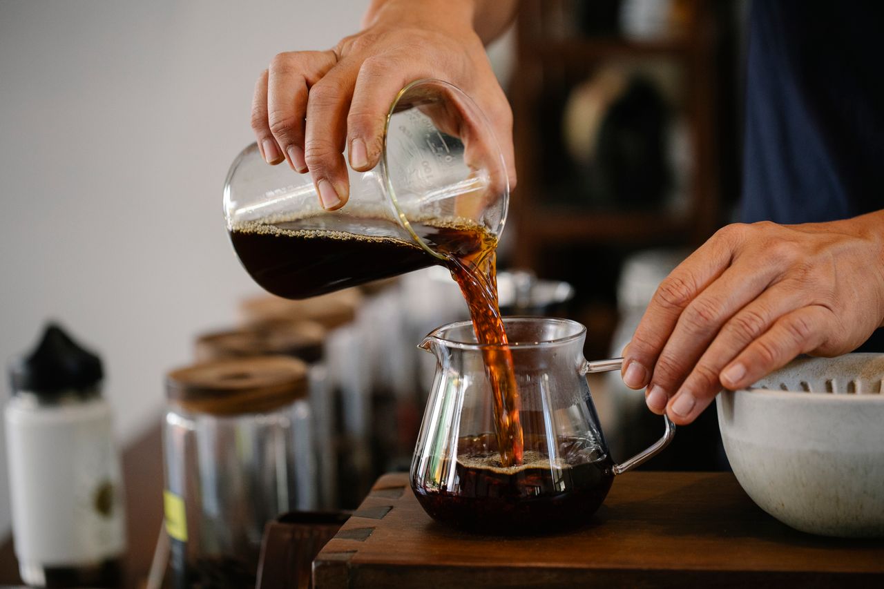 Close-up-barista-menuangkan-kopi-segar-ke-dalam-teko-kaca-di-sebuah-kafe
