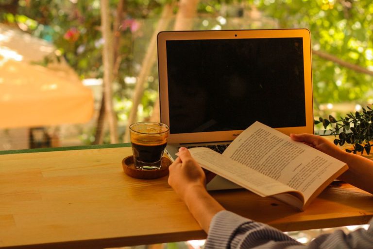 Orang-yang-menikmati-buku-dan-kopi-di-luar-ruangan-dengan-laptop
