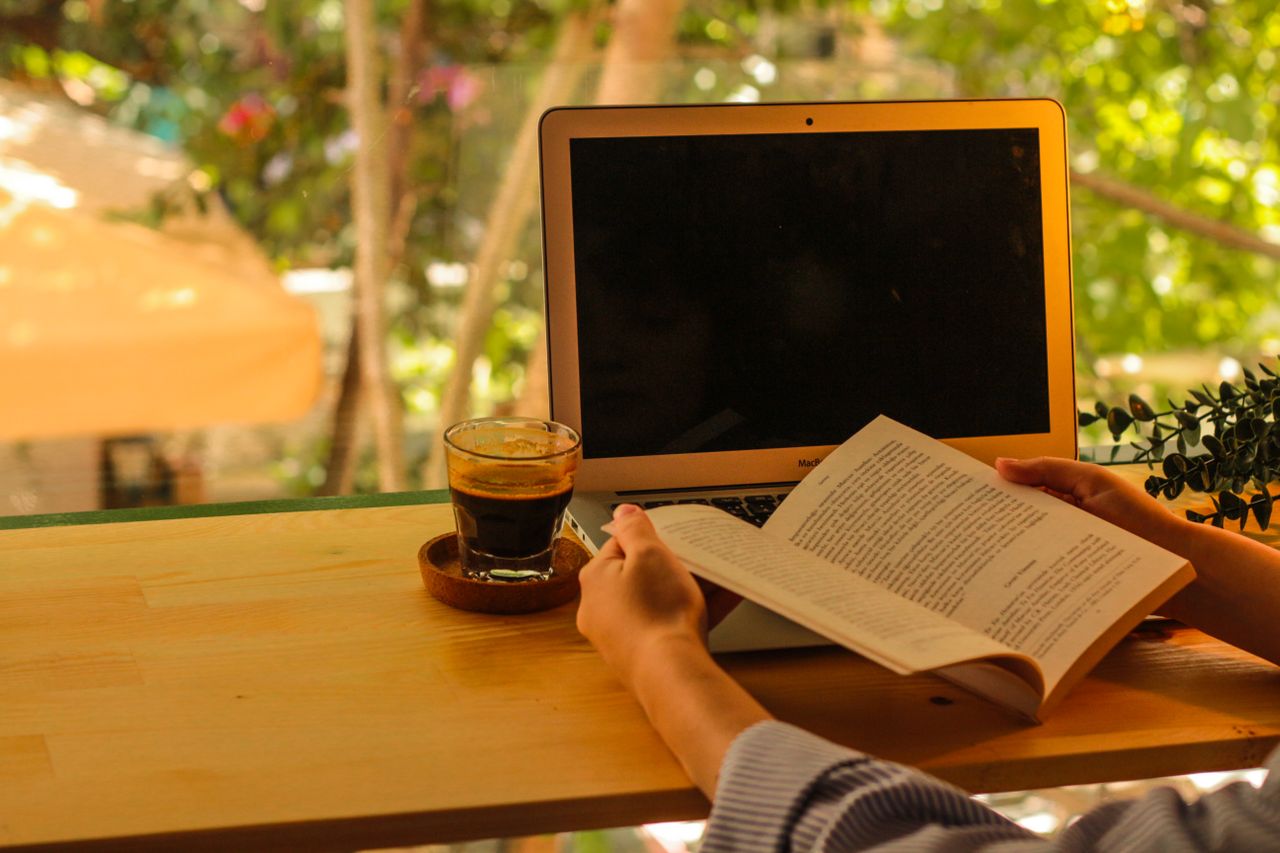 Orang-yang-menikmati-buku-dan-kopi-di-luar-ruangan-dengan-laptop