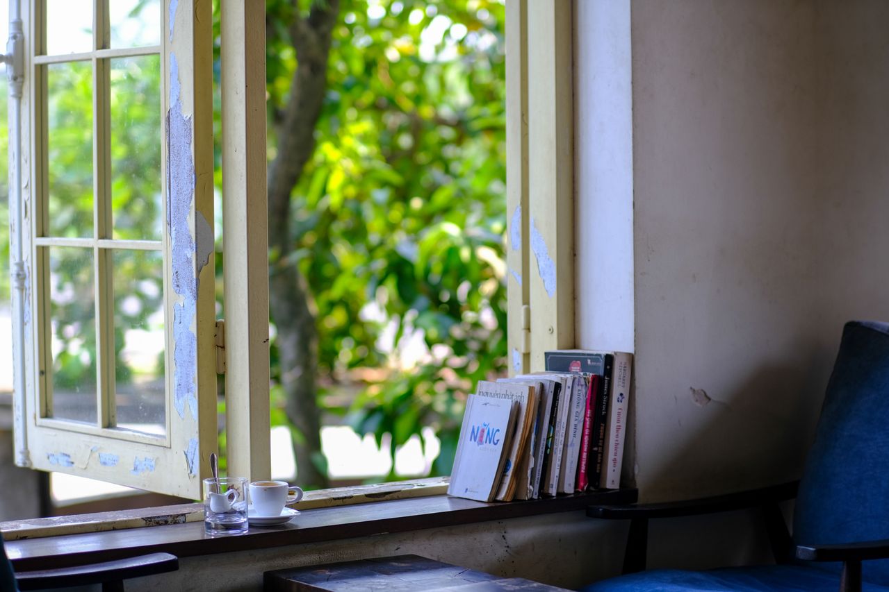 udut-tenang-di-kafe-Vietnam-dengan-buku-kursi-dan-jendela-terbuka-yang-menghadap-tanaman-hijau