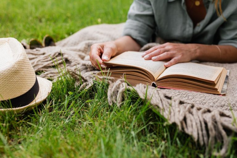 wanita-membaca-buku-di-luar-ruangan-di-atas-selimut-santai-di-atas-rumput